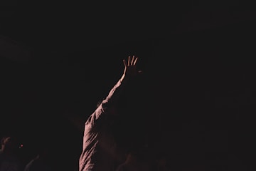 person wearing brown long-sleeved shirt raising right hand while standing