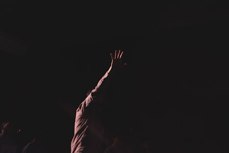 person wearing brown long-sleeved shirt raising right hand while standing