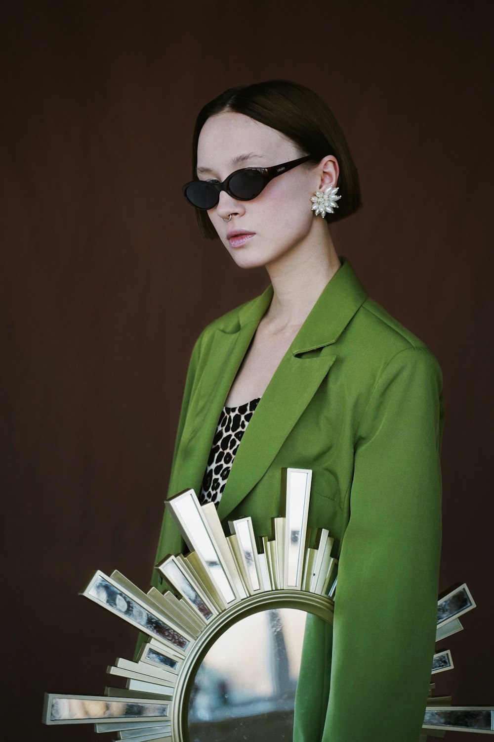woman wearing green notched lapel suit jacket, sunglasses, and white earring standing