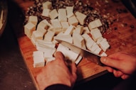 a person chopping cheese on a cutting board with a knife