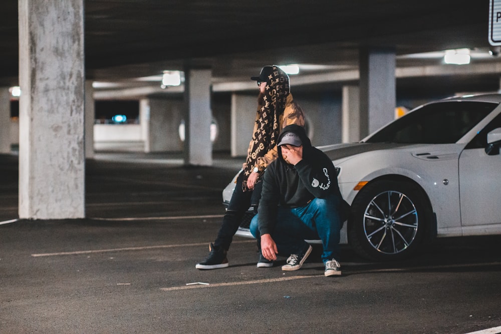 man crouching beside man sitting on car's hood