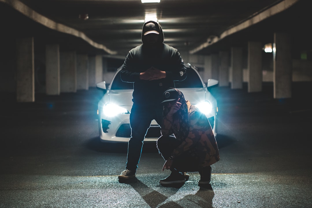 two men standing and crouching in front of car