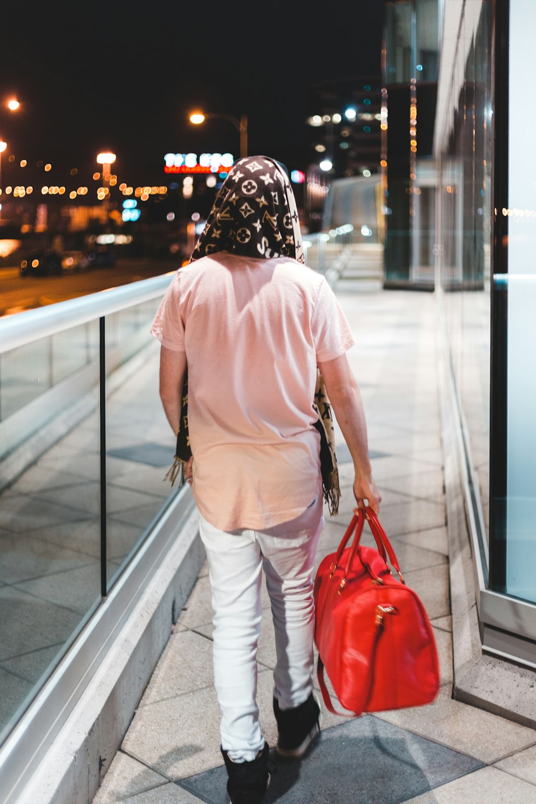 man wearing brown shirt walking holding red duffel bag