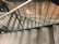 A staircase constructed with metal railings and stone steps, enclosed by a brick wall with visible pattern variations. A safety exit sign is seen on the left, and a wall-mounted notice is in the distance.