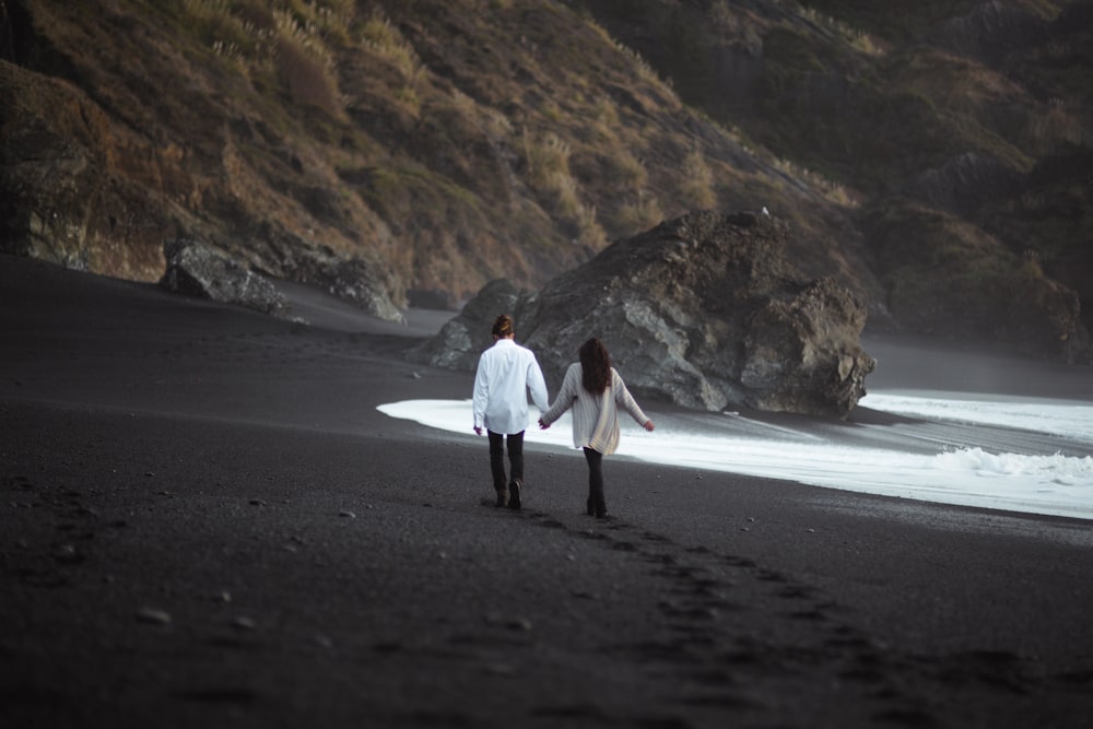man and woman holdings hand together while walking on beach