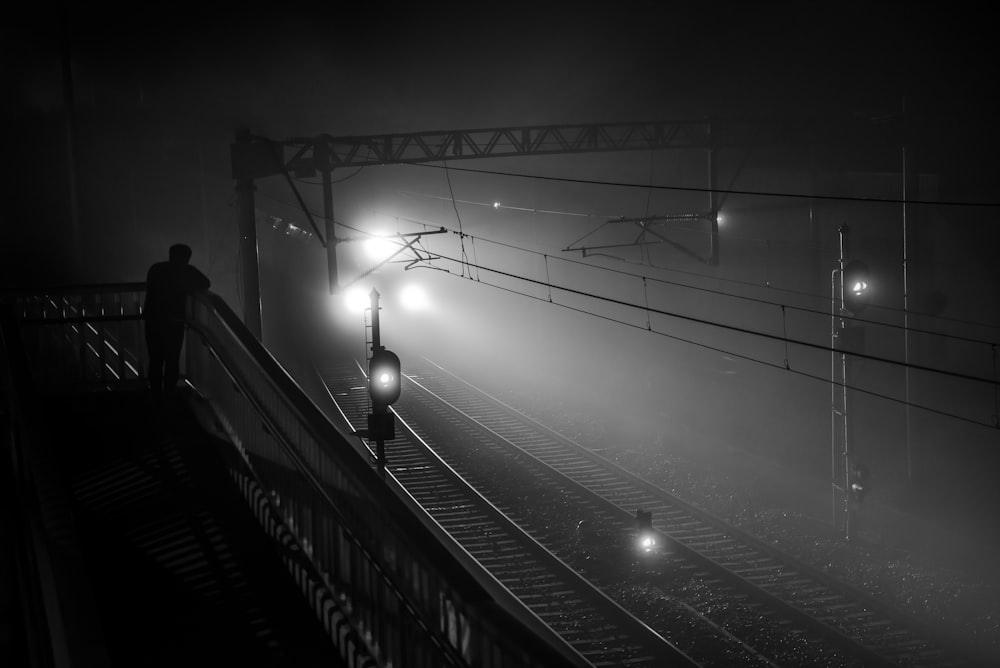 grayscale photography of person standing on stairs looking at railway