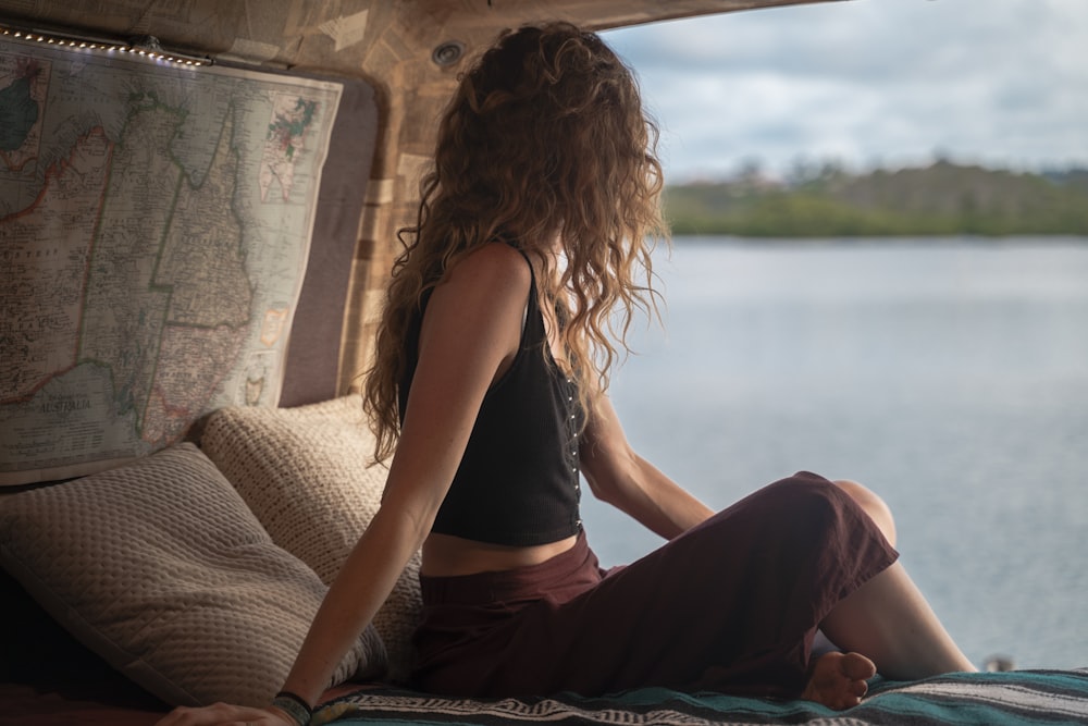 woman wearing black spaghetti strap top sitting viewing body of water