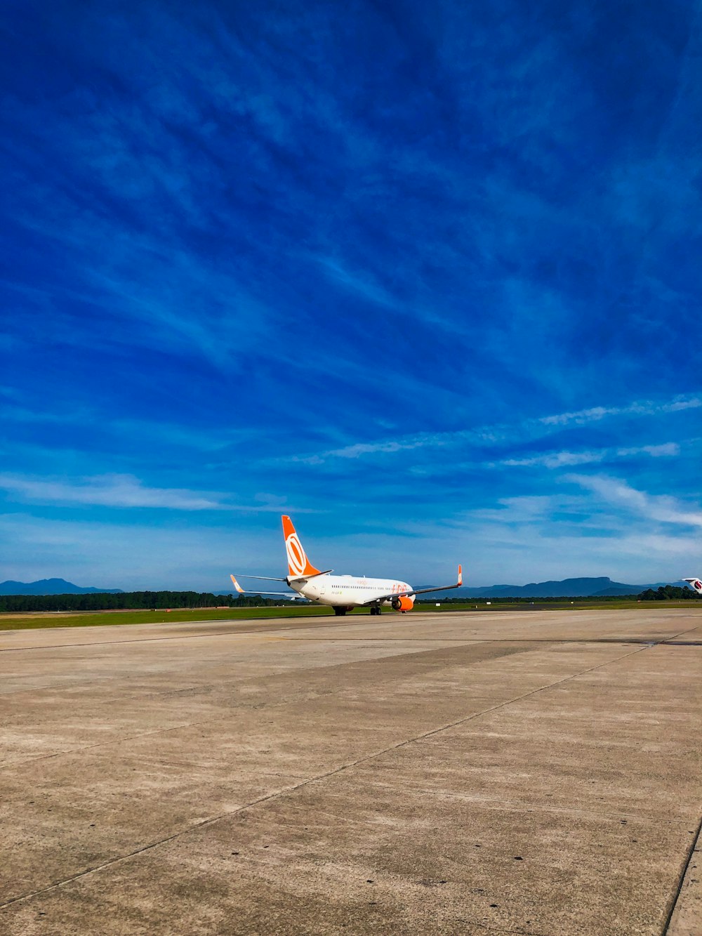 Avión de pasajeros blanco y naranja aterrizando bajo cielo azul y blanco