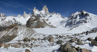 rock formations on field and mountain covered with snow under blue sky