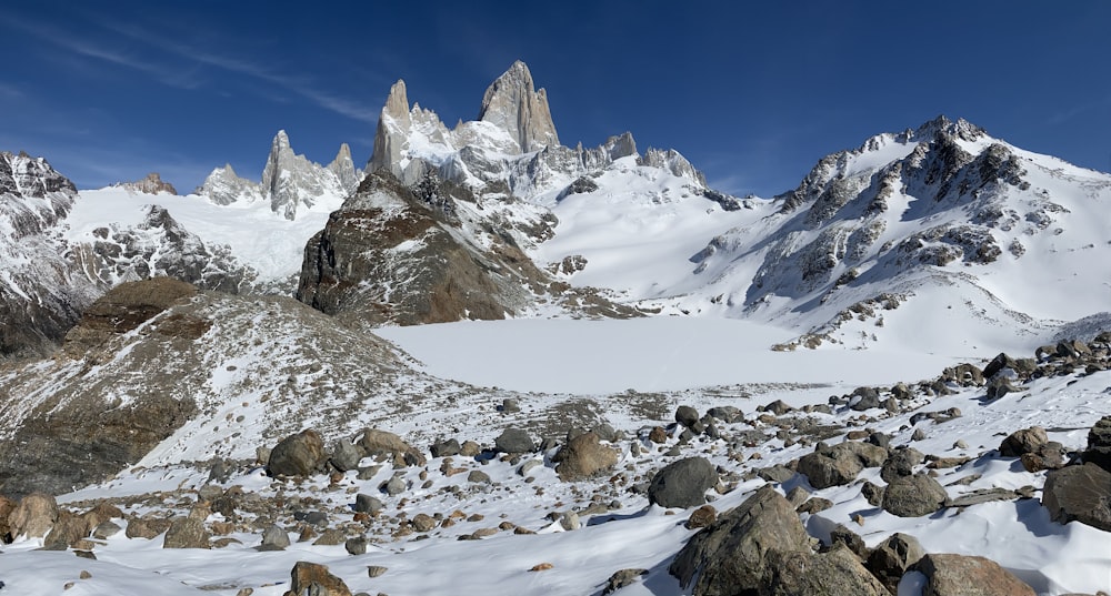 rock formations on field and mountain covered with snow under blue sky
