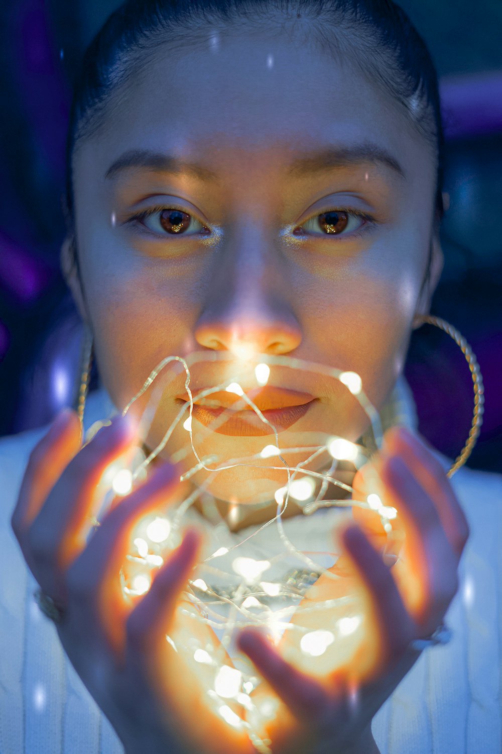 woman wearing white top and gold-colored hoop earrings holding lighted white string lights