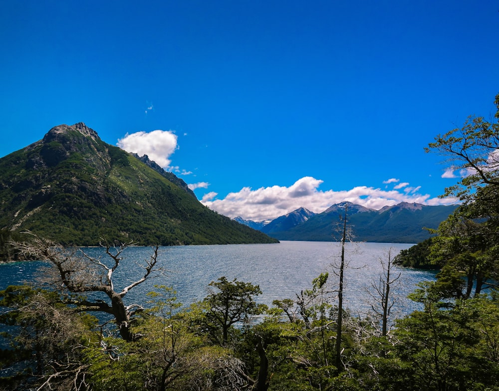 landscape photography of blue body of water viewing mountain under white and blue sky