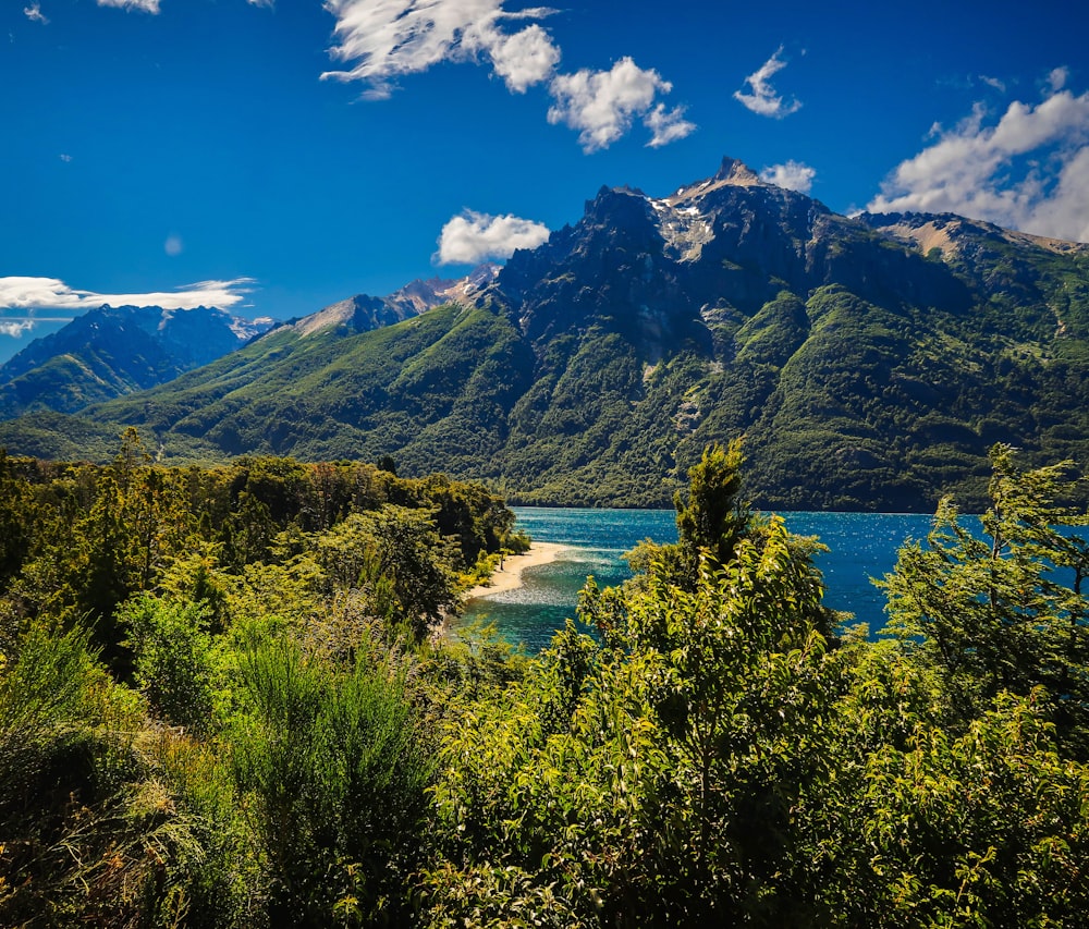 landscape photography of blue body of water viewing mountain under blue and white sky