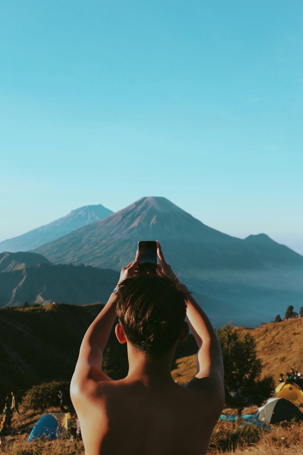 topless man taking photo of mountain under blue and white sky