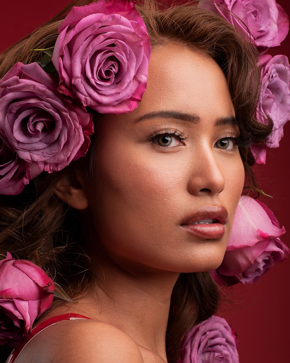portrait photography of woman wearing red spaghetti strap top with purple rose flowers on hair