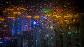 Close-up of raindrops on a windowpane with blurred city lights in the background, evoking a modern climate moment.