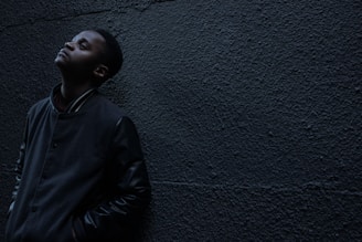 man wearing black button-up jacket standing and leaning against the wall while looking up