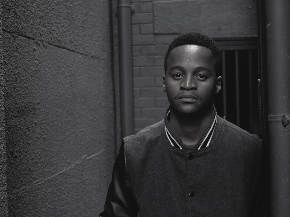 grayscale photography of man standing by concrete wall