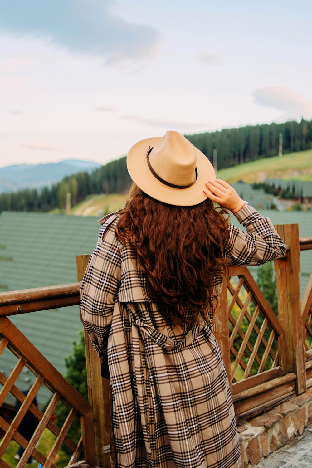 woman wearing brown and black plaid jacket and brown hat standing while facing near railings