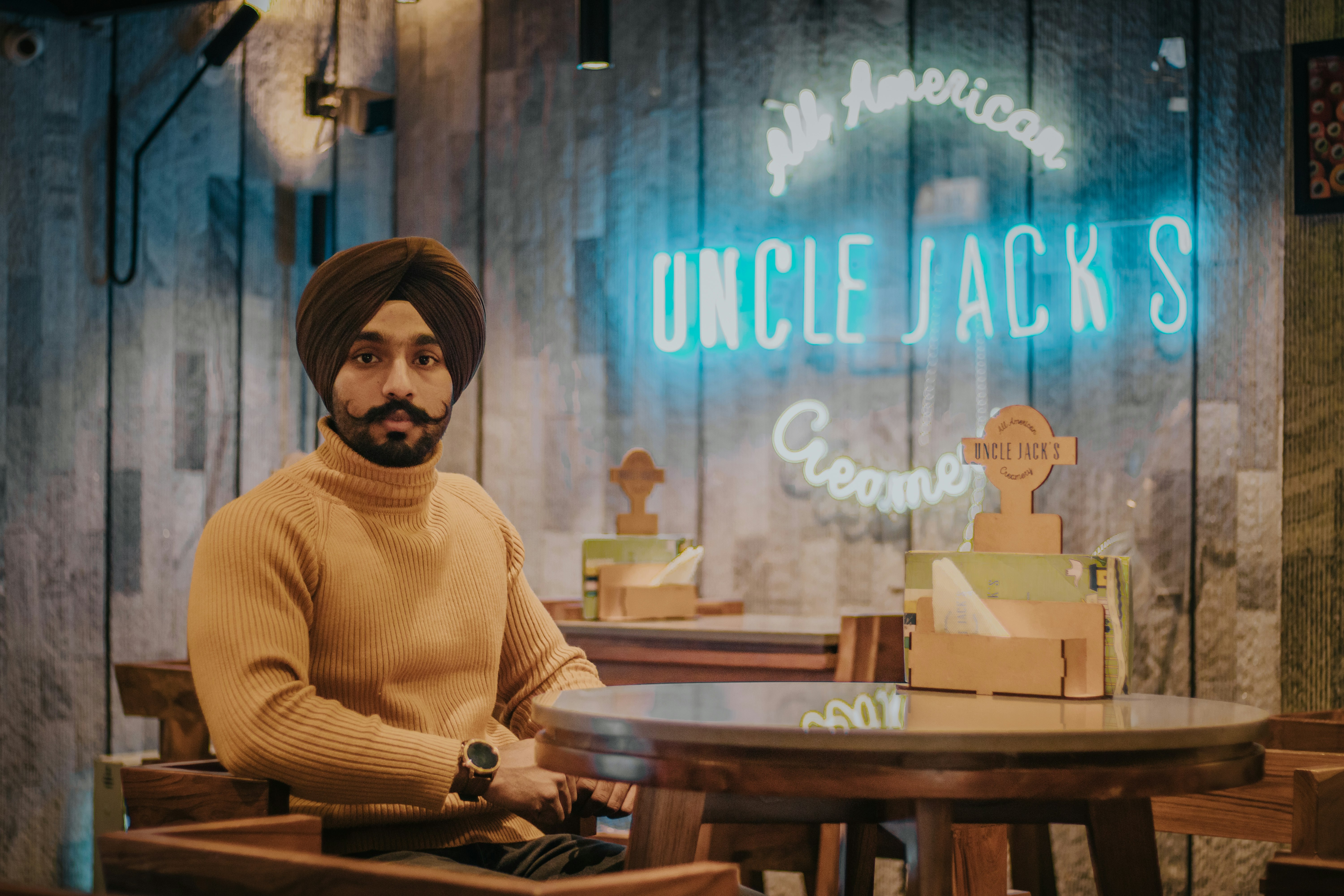 selective focus photography of man sitting beside Uncle Jack's sign