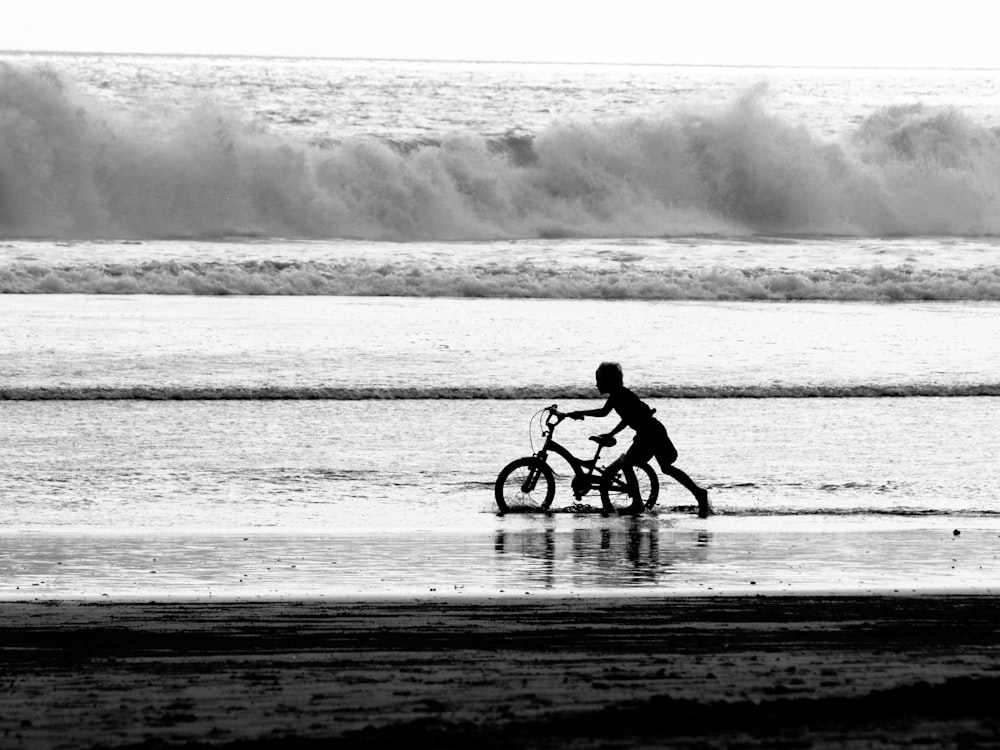 boy pulling bicycle on lake during daytime