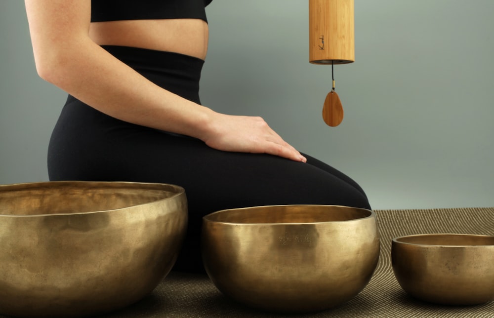 woman kneeling beside three brass-colored bowls