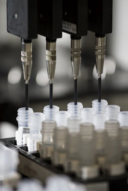 Four metal needles dispensing liquid into small plastic vials in a laboratory