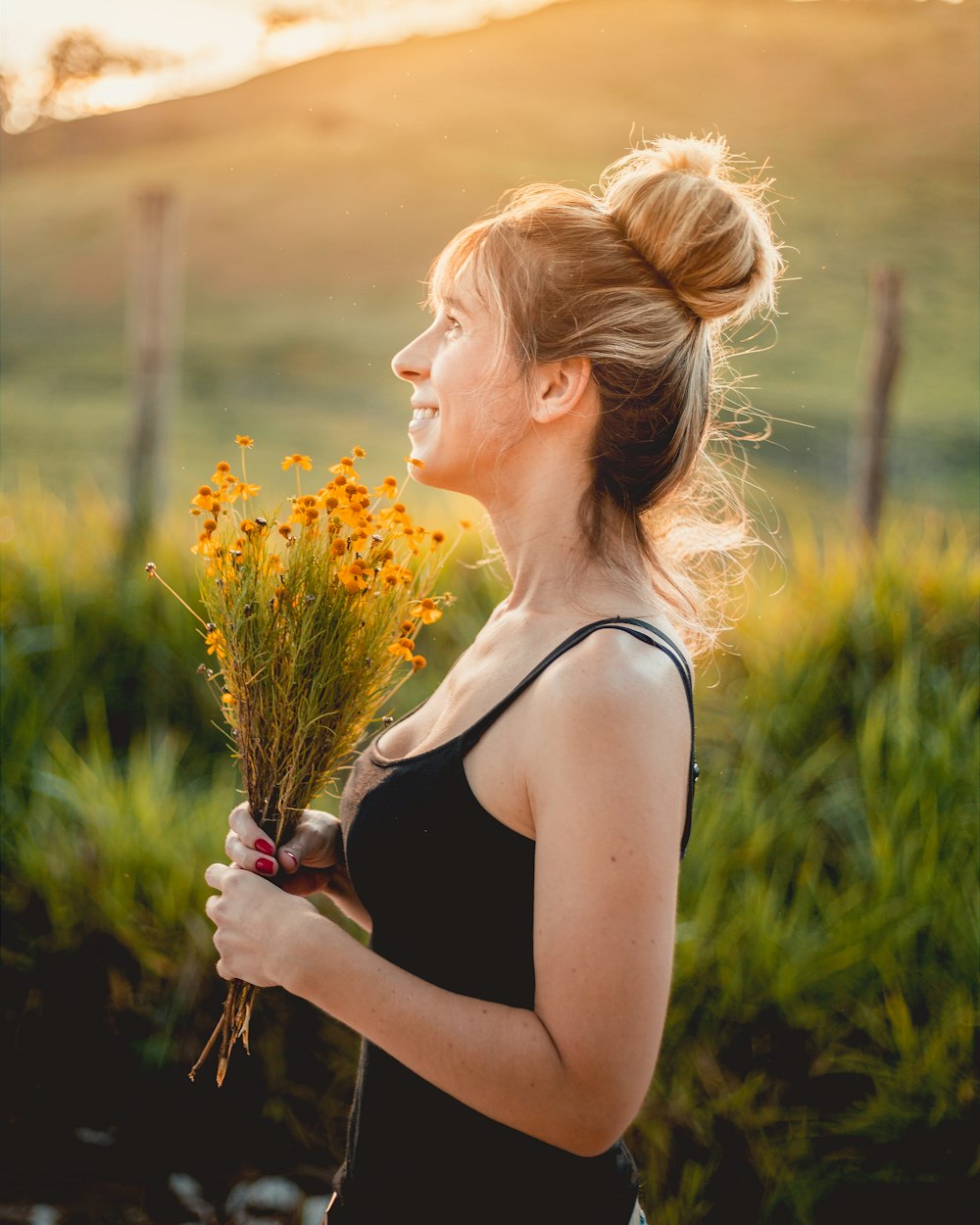 woman in black spaghetti strap top holding yellow flowers outdoors