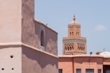 A traditional Moroccan building with decorative towers stands against a clear blue sky. The architecture features intricate designs and earthy tones typical of North African structures.