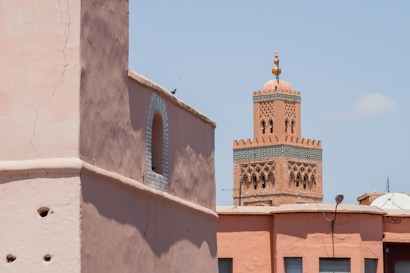 A traditional Moroccan building with decorative towers stands against a clear blue sky. The architecture features intricate designs and earthy tones typical of North African structures.