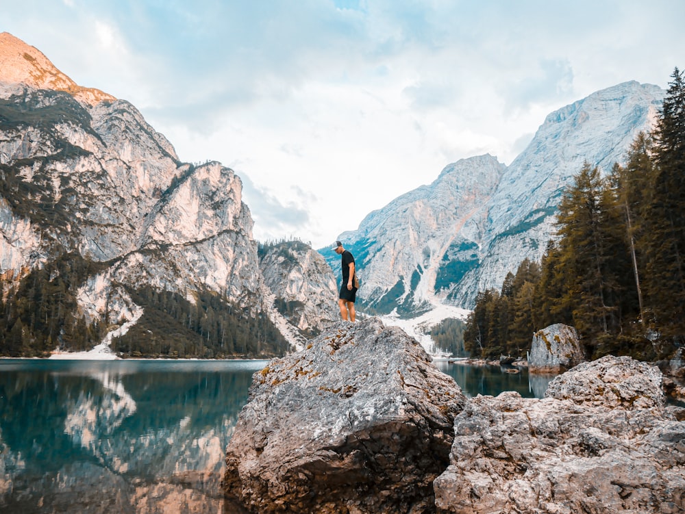 man standing on the rock near calm water of river