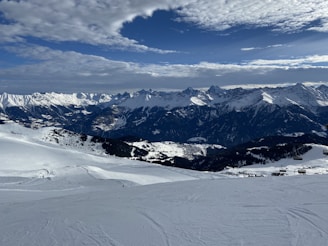 Wide shot of a snowy mountain range at sunrise with ski tracks visible.