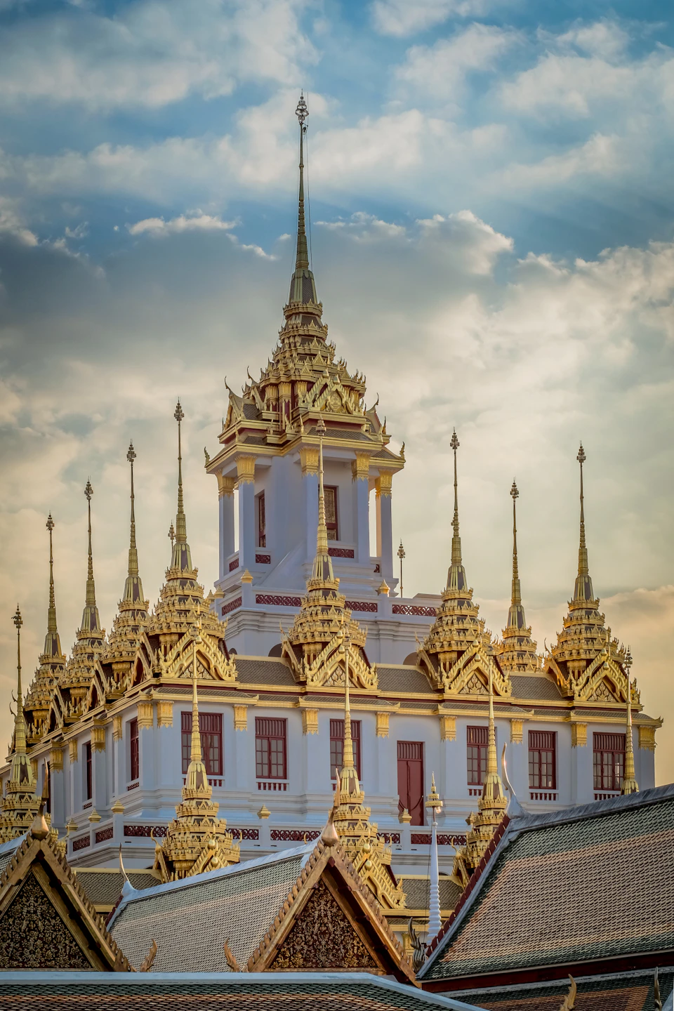 Wat Arun (Temple of Dawn) in Bangkok: white and gold porcelain-inlaid central prang reaching into a clear blue cool-season sky, with the Chao Phraya River in the foreground