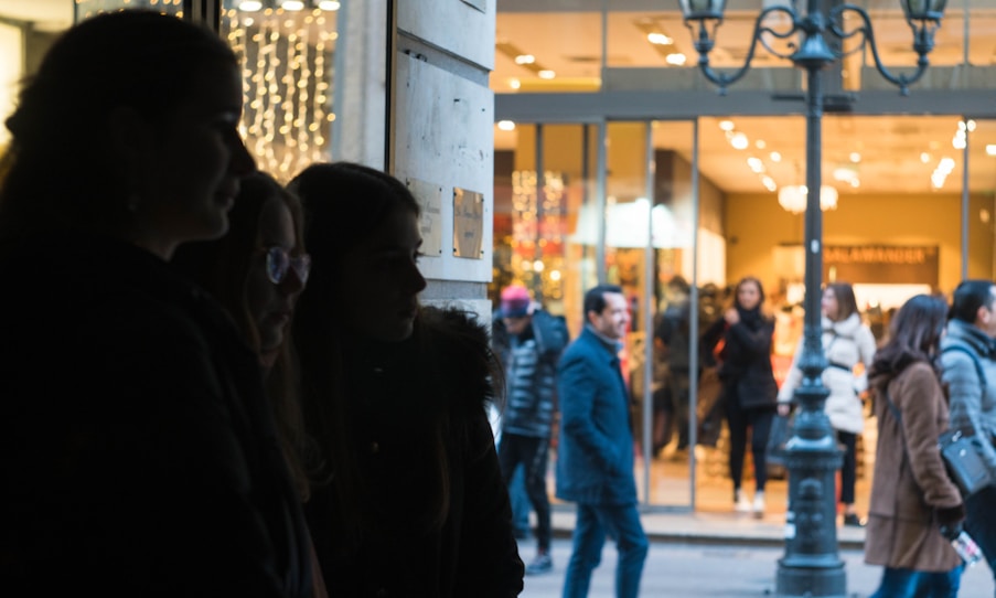 Agent discreetly observing a crowded urban street from a shaded corner.