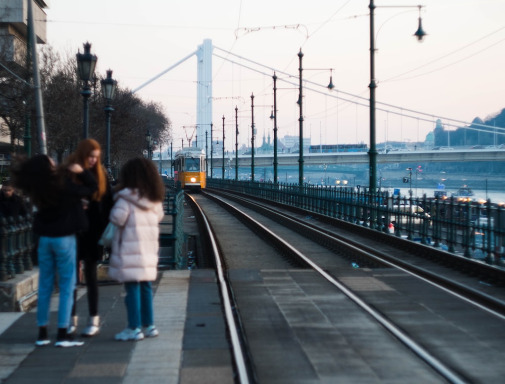 three person standing beside train rail