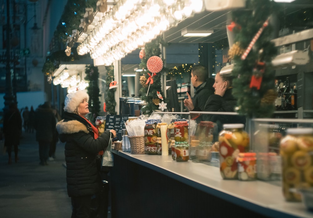 woman in black and white winter coat standing beside stall during nighttime