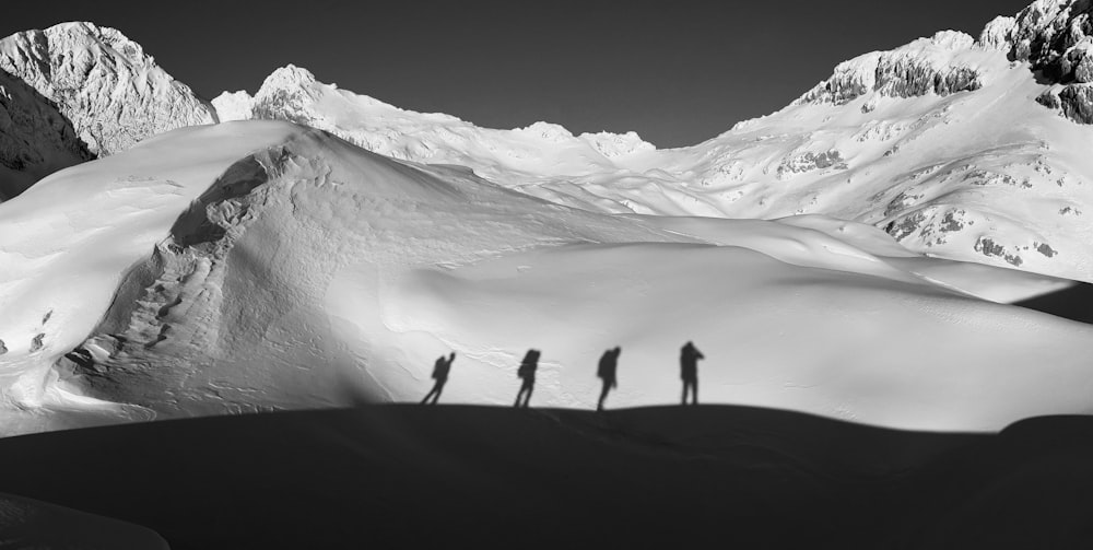 grayscale photography of four people walking near snowy mountain