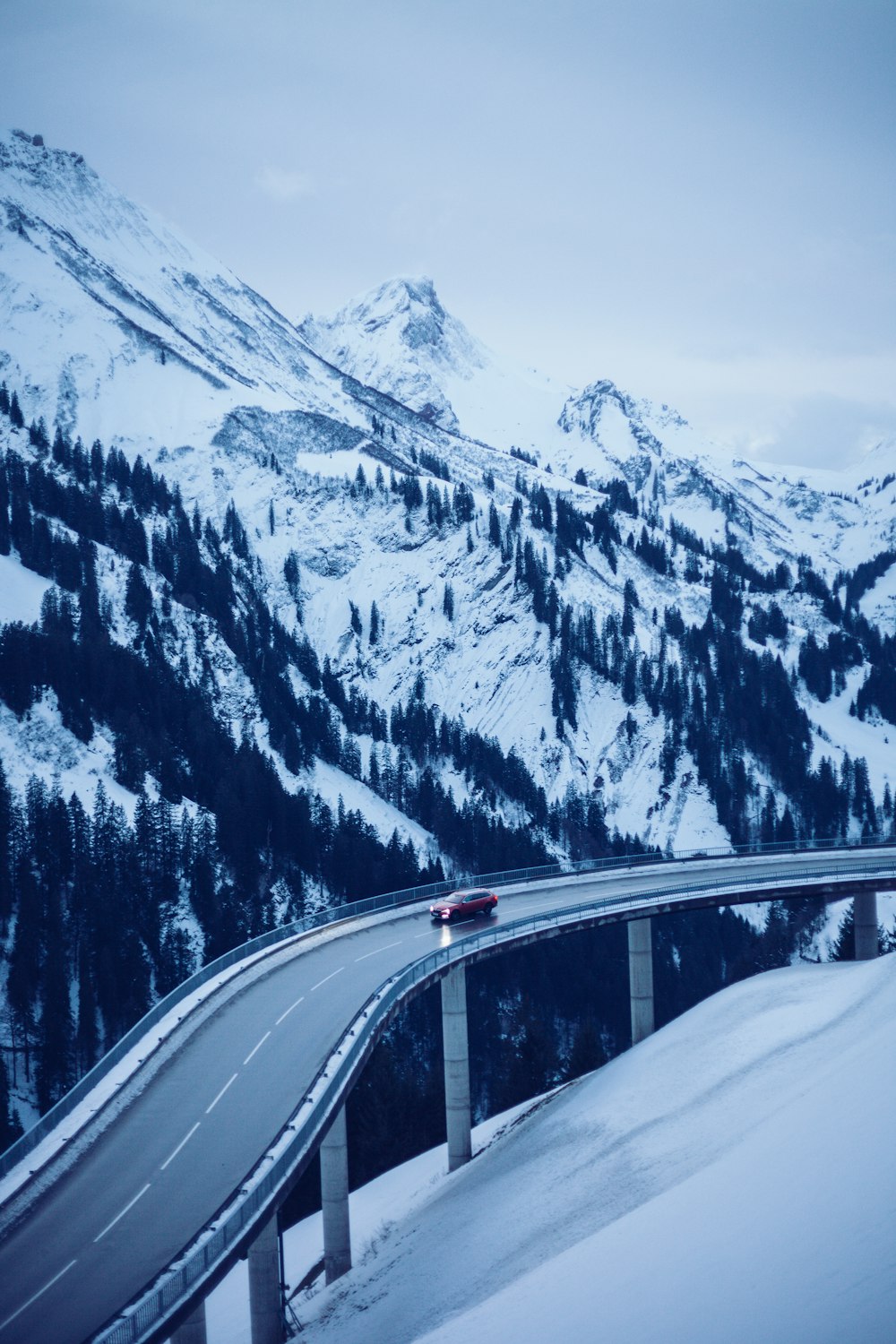 red vehicle on road viewing mountain and trees covered with snow under white and blue sky