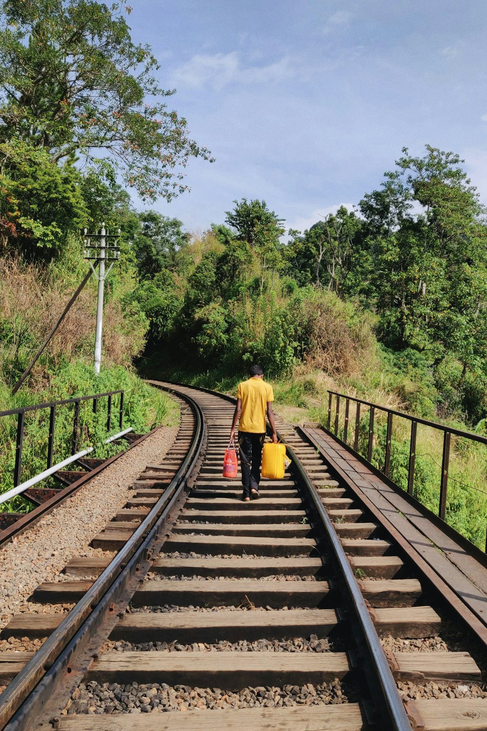 person holding two bags walking on railway during daytime