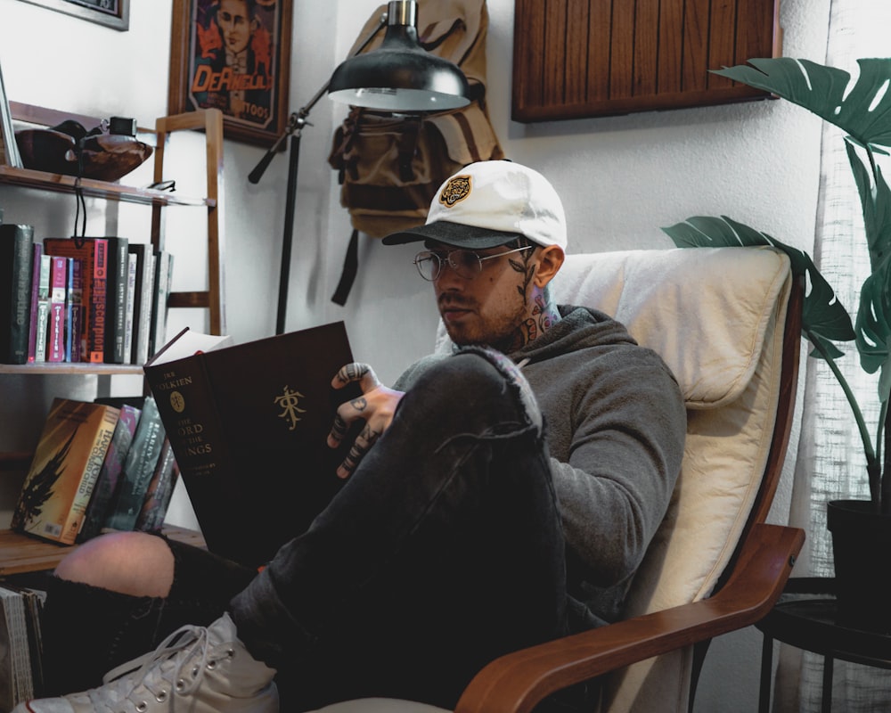 man wearing gray hooded jacket and eyeglasses sitting while reading book