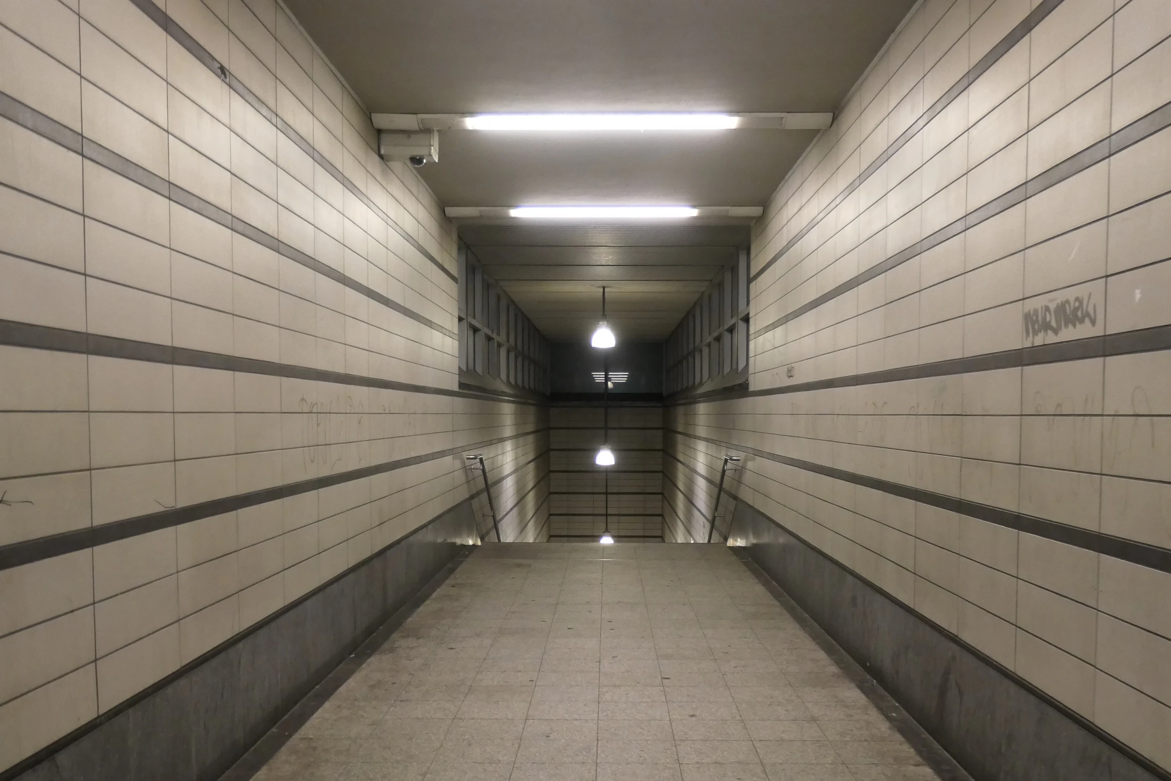A tiled underground passageway, its lines and lights converging to a single point in the distance