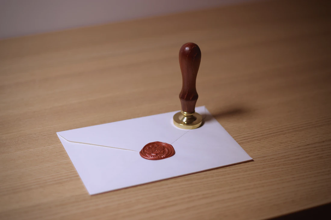 Siegelstempel mit Holzgriff steht auf einem weißen Umschlag mit geprägtem Wachssiegel