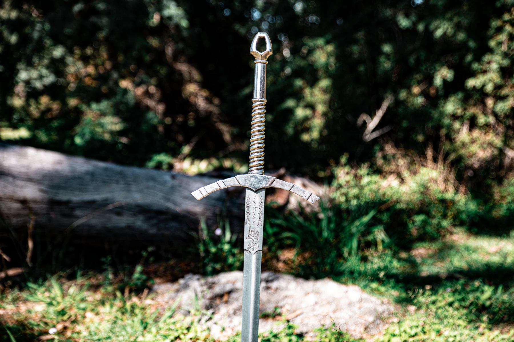 A longsword with a wire-wrapped grip standing point down on a rock in woodland