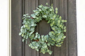 A close-up of a lush, custom-made wreath featuring eucalyptus and soft pink blooms hanging on a rustic wooden door.
