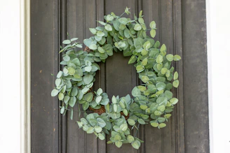 A close-up of a lush, custom-made wreath featuring eucalyptus and soft pink blooms hanging on a rustic wooden door.