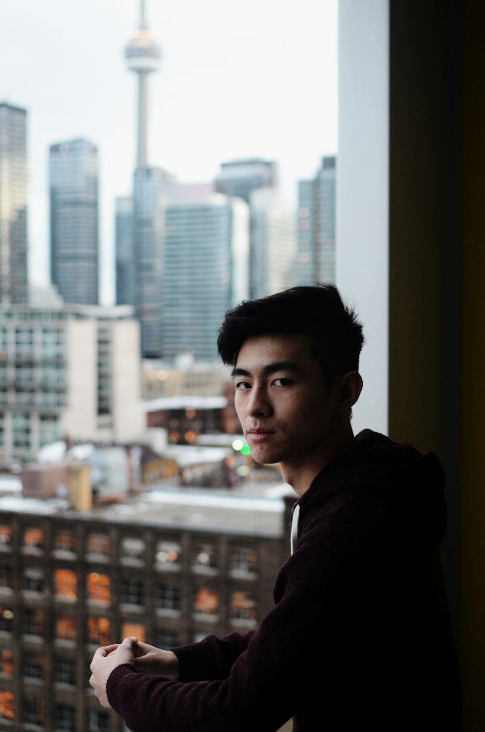 man looking at the camera beside window at the city during day