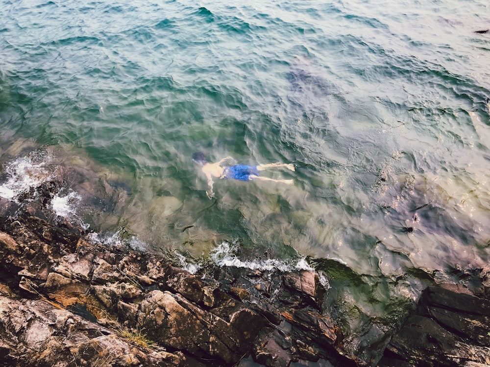 man in blue short swimming on seashore during daytime