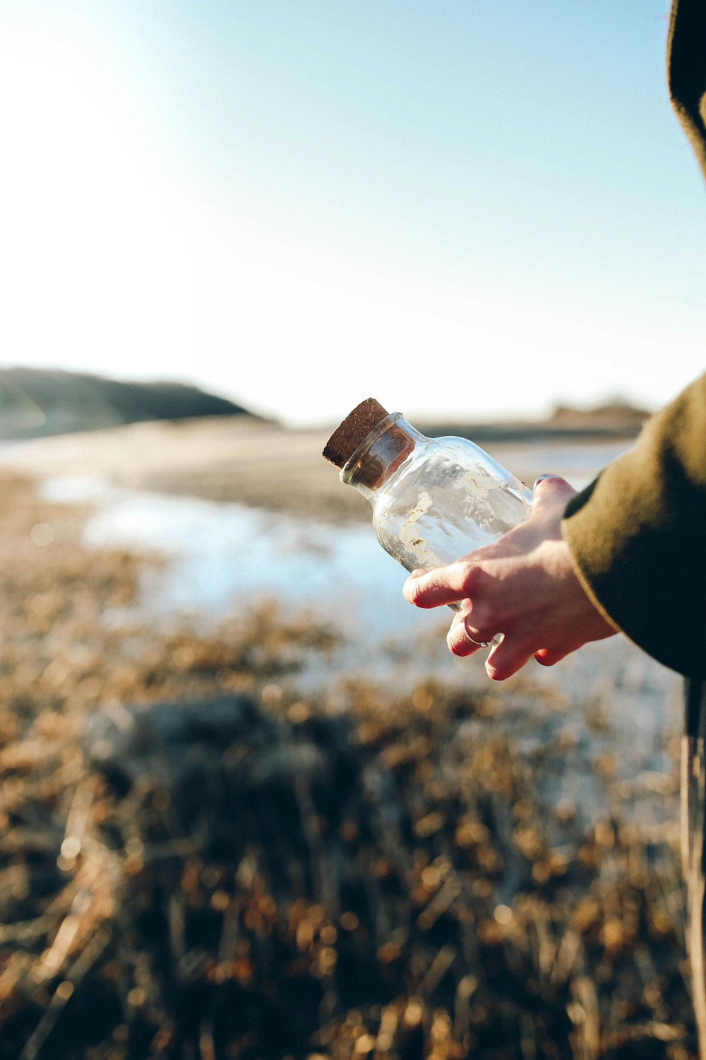 foto con messa a fuoco superficiale di una persona che tiene una bottiglia di vetro trasparente