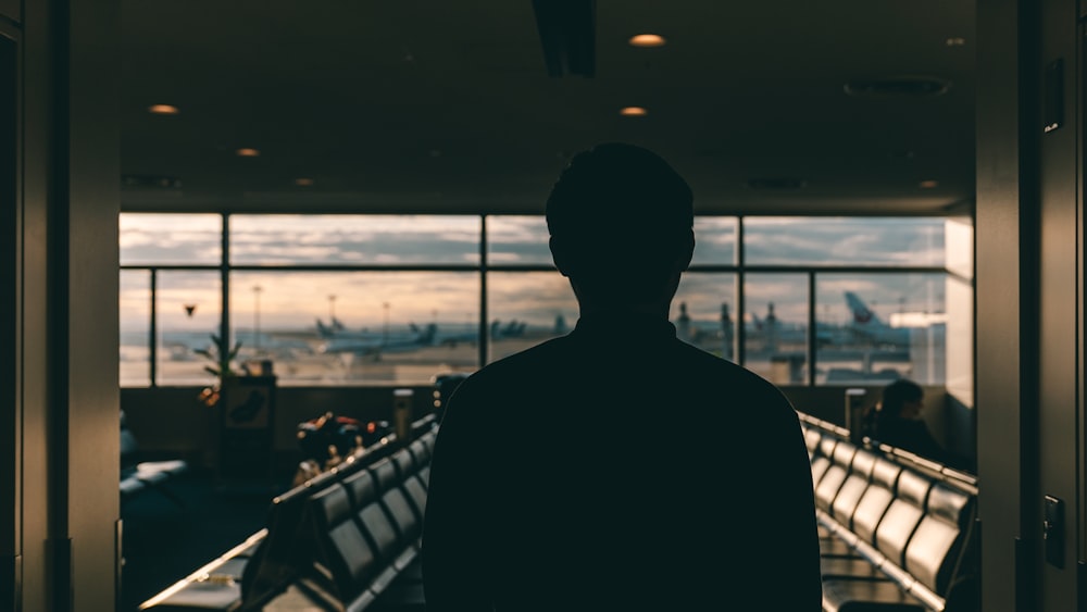 a man standing in front of a window looking out at an airport