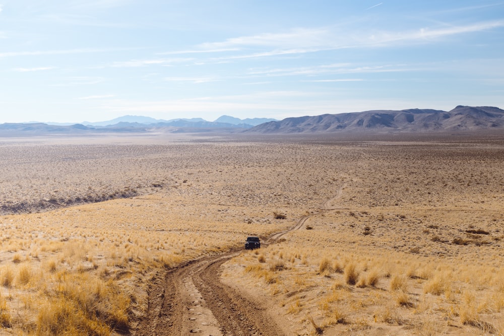 wide-angle photography of black vehicle traveling on desert during daytime